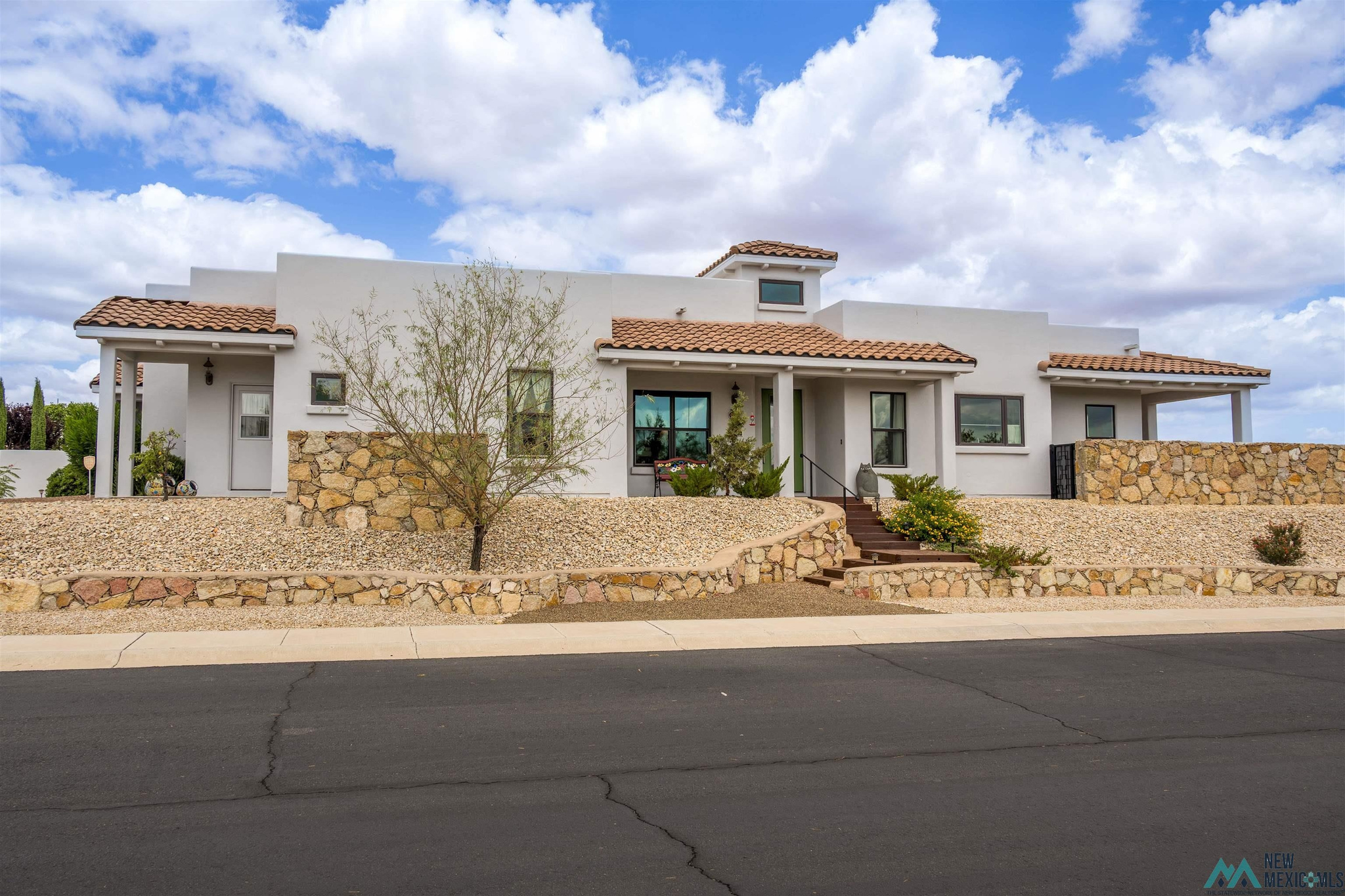 Modern white stucco home with terracotta tile roofs, stone walls, and a gravel front yard.